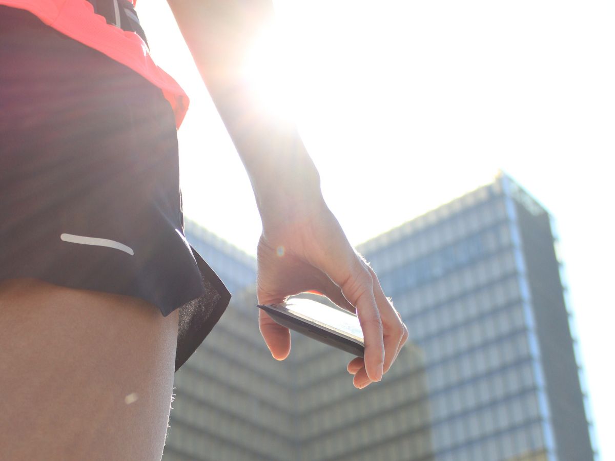 Coureuse en tenue légère courant au lever du soleil avec une ceinture de running contenant une petite gourde, symbole de l’hydratation estivale.