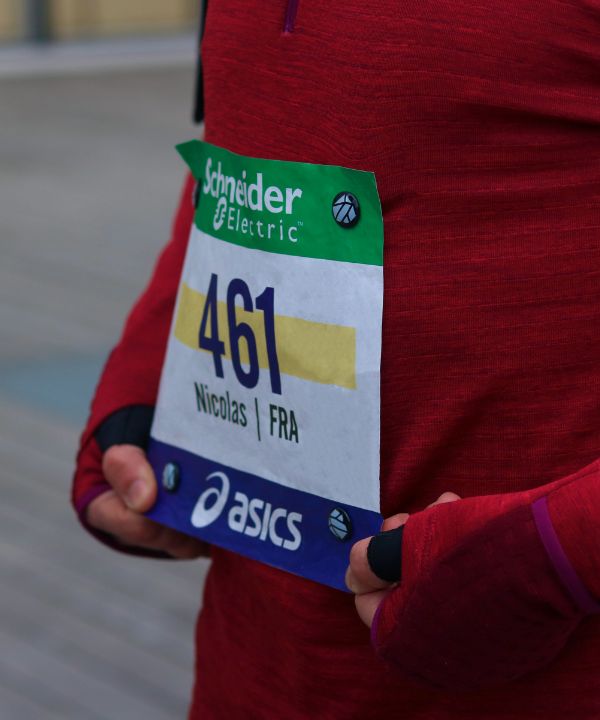 Athlète au départ d’une compétition portant un dossard maintenu par des aimants sur un t-shirt technique, illustrant la préparation optimale pour une course officielle.