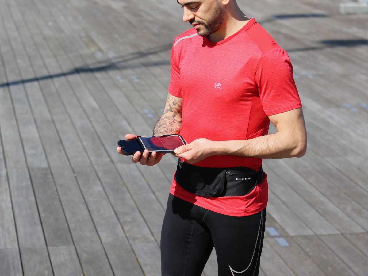 Joggeur en veste imperméable courant sous la pluie avec un brassard étanche visible sur le bras, illustrant la protection des objets électroniques en course.